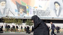 سيدة إيرانية تسير بجانب جدارية لمرشدي الثورة الإيرانية الخميني والخامنئي- جيتي