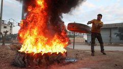 رجل يحرق الإطارات في محاولة لعرقلة الغارات الجوية وسط اشتباكات في إدلب - جيتي