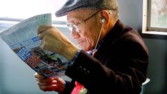 عجوز يستمع لموسيقى ويقرأ جريدة - جيتي