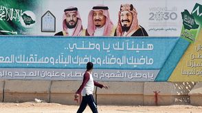 سعودي يسير بجانب لافتة لرؤية 2030 في الرياض- جيتي