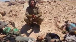 أحد عناصر داعش يلتقط صورة بجانب جثث قتلى للنظام في حقل الشاعر - أرشيفية