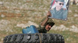 أحد جنود النظام يرفع صور الأسد- جيتي