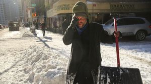 رجل أميركي يزيل الثلج من على الأرصفة في أحد الشوارع بنيويورك - ا ف ب