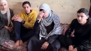 ملتحفة بالشماغ الفلسطيني بينما جلس أبناؤها بجانبها على قطعة أثاث بالية- يوتيوب