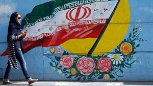 فتاة إيرانية ترتدي زيا غير التقليدي المفروض تمر بجانب جدارية في طهران- جيتي