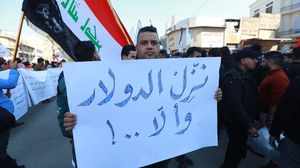 عراقي يرفع لافتة احتجاج خلال تظاهرة على أزمة الدولار في بغداد- الأناضول