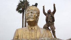 أحد الثوار يعتلي تمثالاً للرئيس السوري السابق حافظ الأسد في إدلب - وكالات