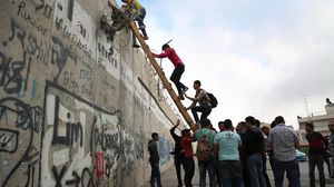 شبان فلسطينيون يستخدمون السلالم الخشبية لتخطي جدار الفصل العنصري - الأناضول