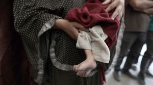 فلسطينية تحمل جثمان طفلها الشهيد جراء تجويعه في قطاع غزة- الأناضول