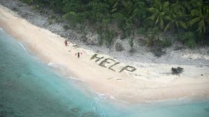 صورة بتاريخ 7 نيسان/ إبريل 2016 لشخصين بجانب عبارة "النجدة" كتباها بأغصان النخيل على جزيرة فاناديك- أ ف ب