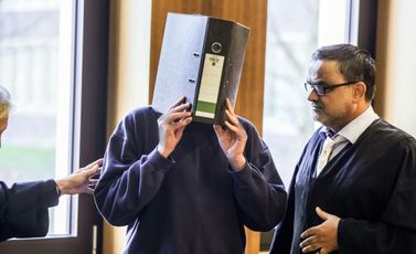 المدعى عليه وهو ممرض سابق يخفي وجهه خلف ملف ويقف بجانب محاميه فولكر بريير خلال وصوله إلى المحكمة في آخن بغرب ألمانيا في 5 تشرين الثاني/نوفمبر 2025